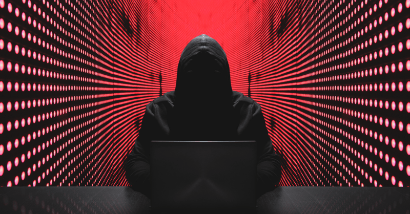 Image shows a cyber hacker's silhouette, with a red background behind them