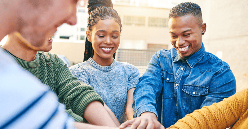 Image of a diverse group of people joining hands, indicating that they work for a company that considers their social value and impact